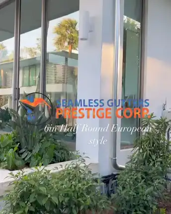 A round downspout running down the corner of a modern glass fronted Miami home, part of a 6 inch half round European profile
