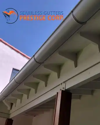 A finished half round gutter running tight along the rafter tails of a tile roofed home against a clear sky