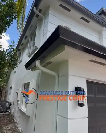 A white gutter and downspout wrapping the corner of a two storey house with dark trim, above the garage