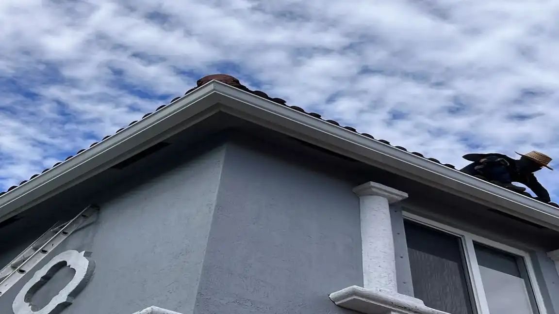 A Prestige installer on a tile roof in South Florida fitting a new white seamless gutter along the fascia